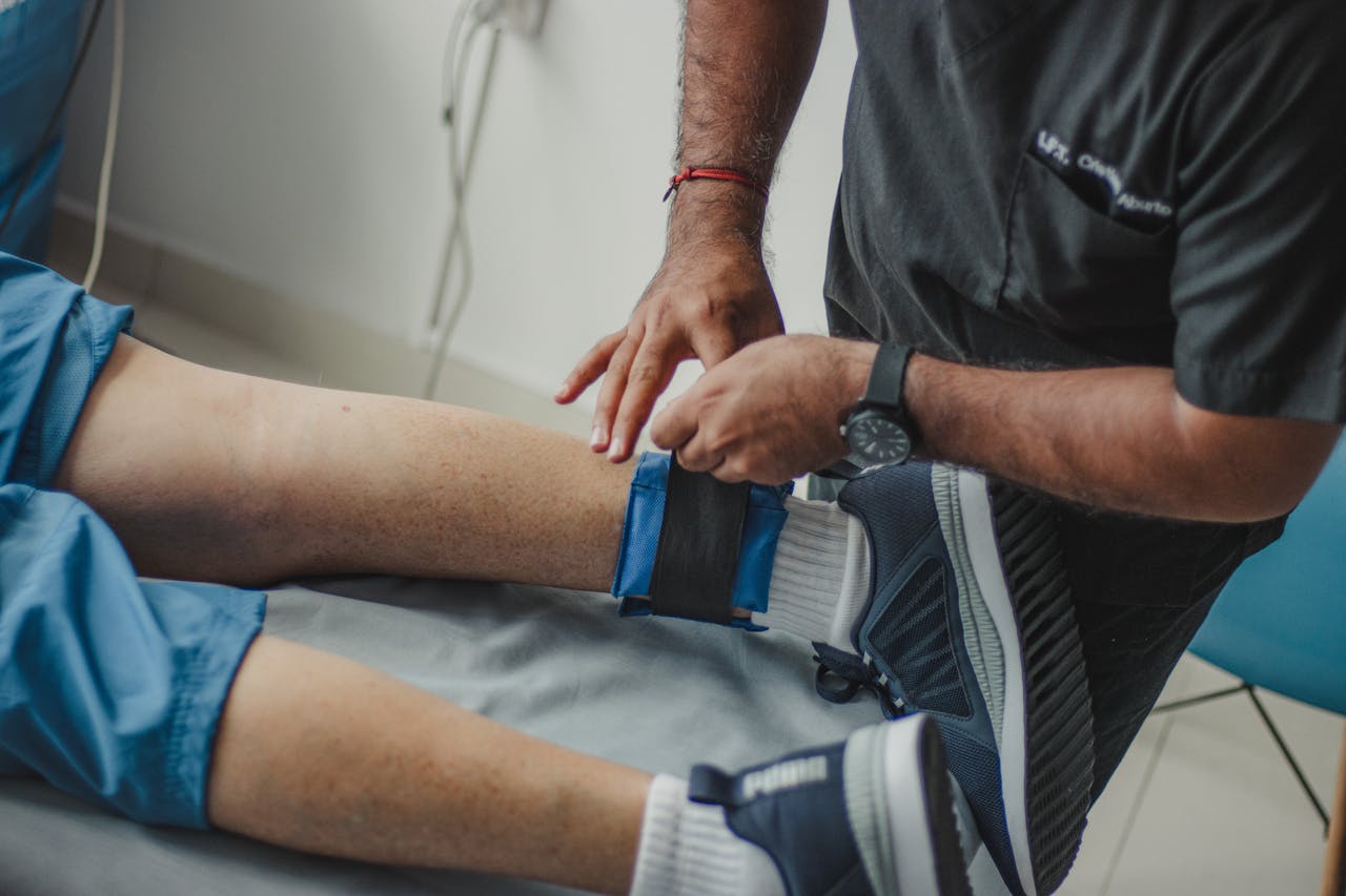 A physiotherapist adjusts a leg strap on a patient in a clinical setting.